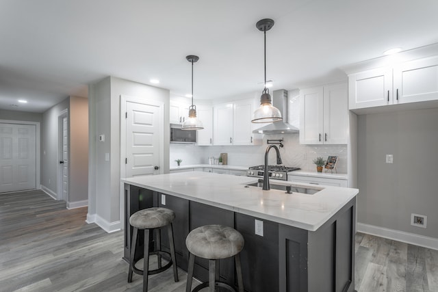 kitchen featuring light stone counters, wall chimney exhaust hood, white cabinetry, and hardwood / wood-style floors