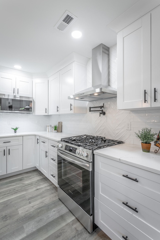 kitchen featuring white cabinets, tasteful backsplash, stainless steel gas stove, wall chimney range hood, and light wood-type flooring