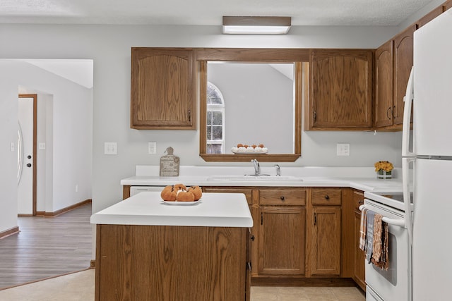 kitchen with a textured ceiling, light wood-type flooring, white appliances, and sink