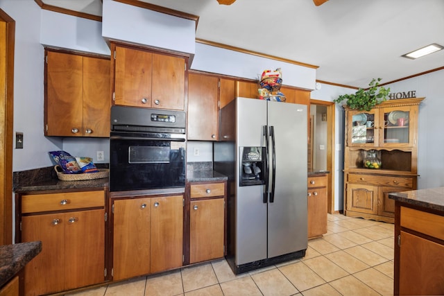 kitchen featuring oven, stainless steel fridge with ice dispenser, dark stone counters, ornamental molding, and light tile patterned floors