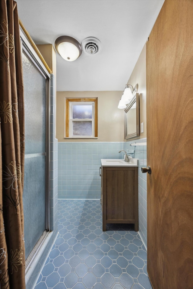 bathroom featuring a shower with door, vanity, tile patterned flooring, and tile walls