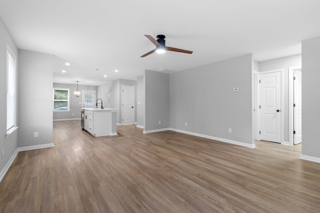 unfurnished living room with ceiling fan with notable chandelier, light wood-type flooring, and sink