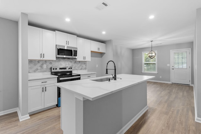 kitchen featuring stainless steel appliances, light hardwood / wood-style flooring, pendant lighting, a kitchen island with sink, and white cabinets