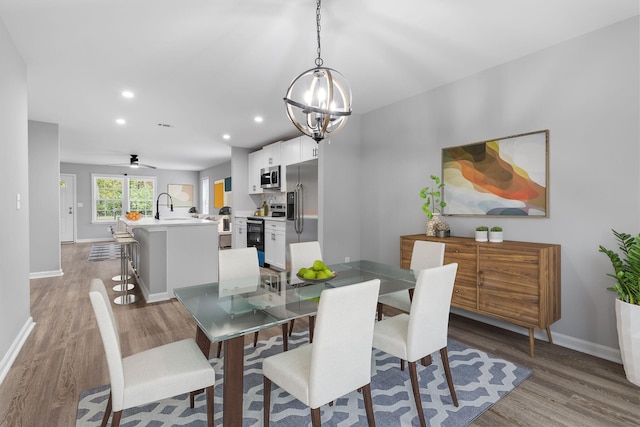 dining room with sink, light hardwood / wood-style floors, and ceiling fan with notable chandelier