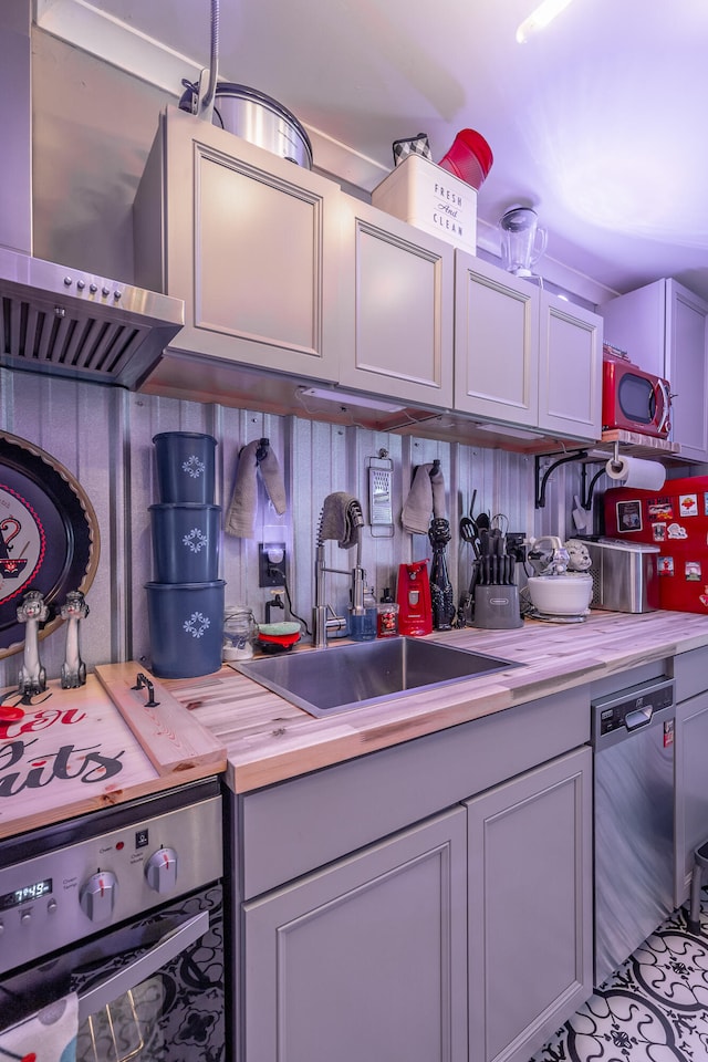 kitchen with stainless steel appliances, wall chimney exhaust hood, sink, and gray cabinets