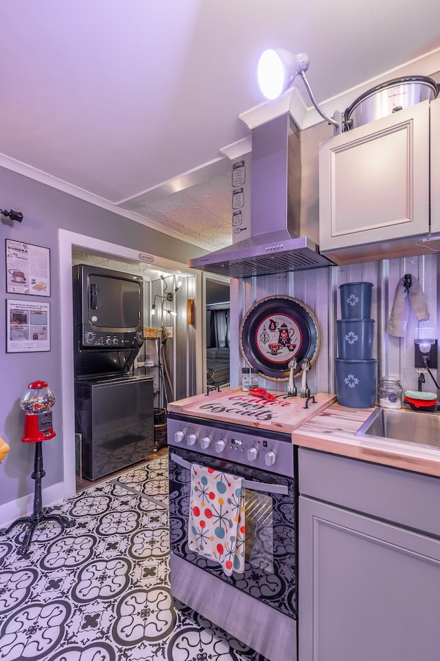 kitchen featuring stainless steel stove, ornamental molding, butcher block counters, gray cabinetry, and wall chimney exhaust hood