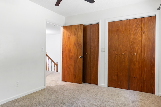 unfurnished bedroom with carpet floors, two closets, a textured ceiling, and ceiling fan