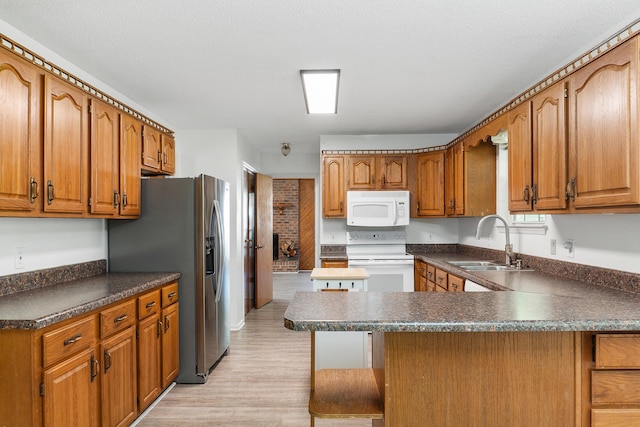 kitchen with white appliances, sink, light hardwood / wood-style floors, a breakfast bar area, and a textured ceiling