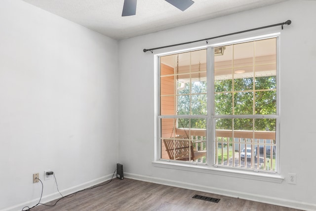 empty room featuring ceiling fan, hardwood / wood-style flooring, a textured ceiling, and a healthy amount of sunlight