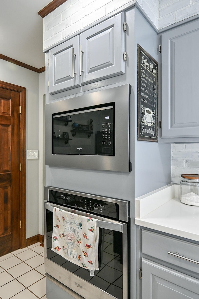 kitchen with light tile patterned floors, ornamental molding, tasteful backsplash, gray cabinetry, and stainless steel appliances