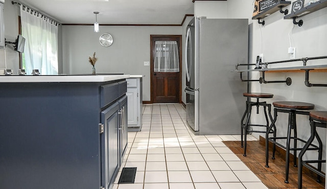 kitchen featuring a kitchen breakfast bar, stainless steel refrigerator, hanging light fixtures, ornamental molding, and light tile patterned floors