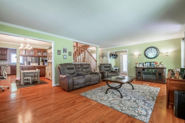 living area featuring a chandelier, crown molding, light wood-style flooring, and stairs