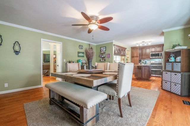 dining space featuring light wood finished floors, ceiling fan, track lighting, baseboards, and ornamental molding
