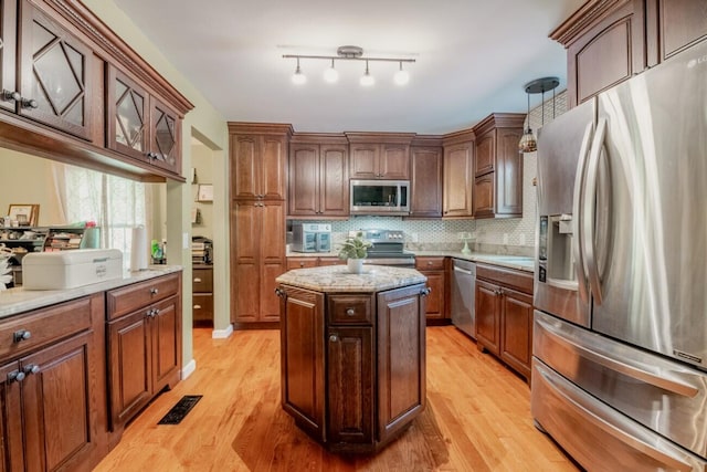kitchen with glass insert cabinets, decorative backsplash, appliances with stainless steel finishes, a center island, and light wood-type flooring