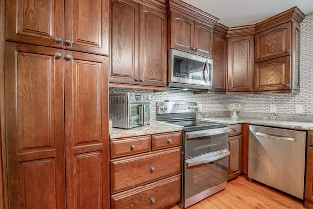 kitchen with backsplash, appliances with stainless steel finishes, light wood-type flooring, and light stone countertops