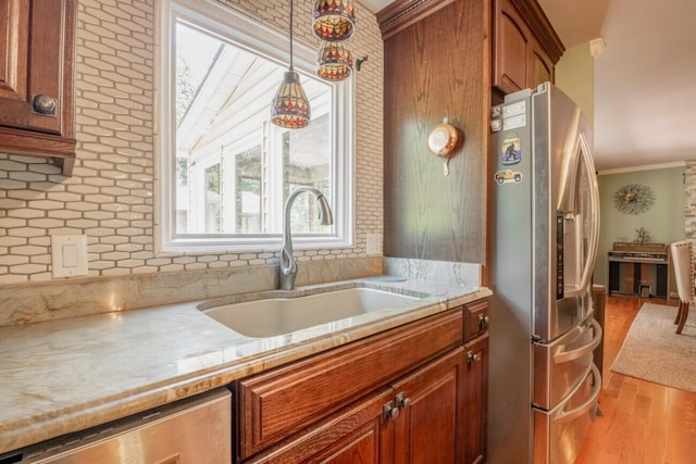 kitchen featuring sink, ornamental molding, hanging light fixtures, light hardwood / wood-style flooring, and appliances with stainless steel finishes