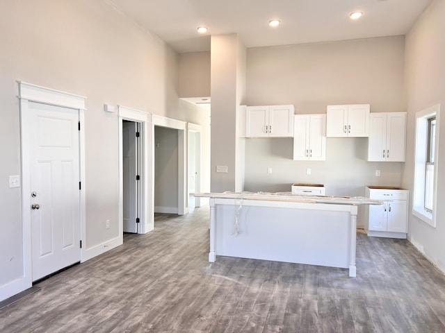 kitchen featuring a towering ceiling, a center island, white cabinetry, and hardwood / wood-style floors