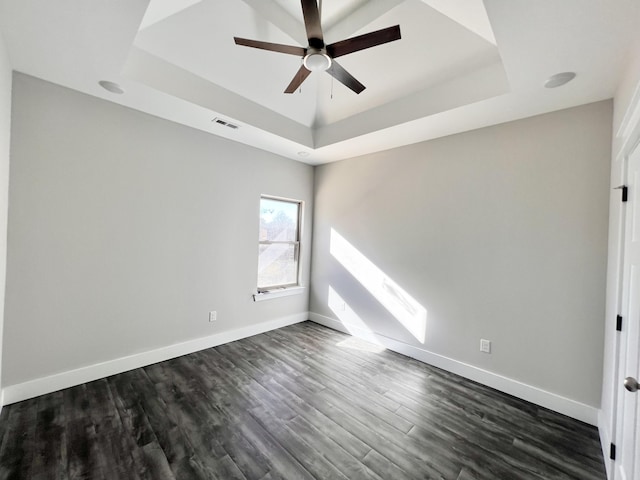 empty room with ceiling fan, dark hardwood / wood-style flooring, and a tray ceiling