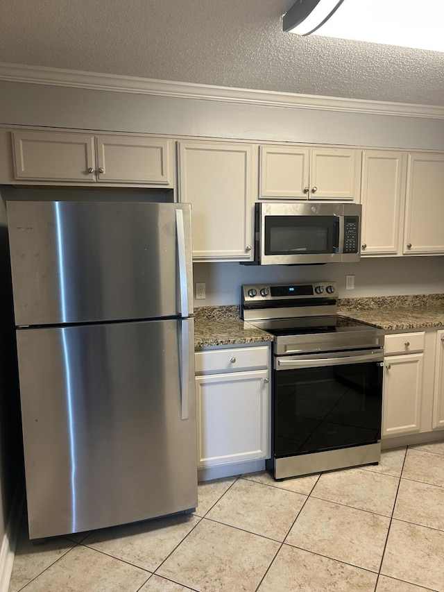 kitchen featuring dark stone counters, a textured ceiling, stainless steel appliances, light tile patterned floors, and white cabinetry