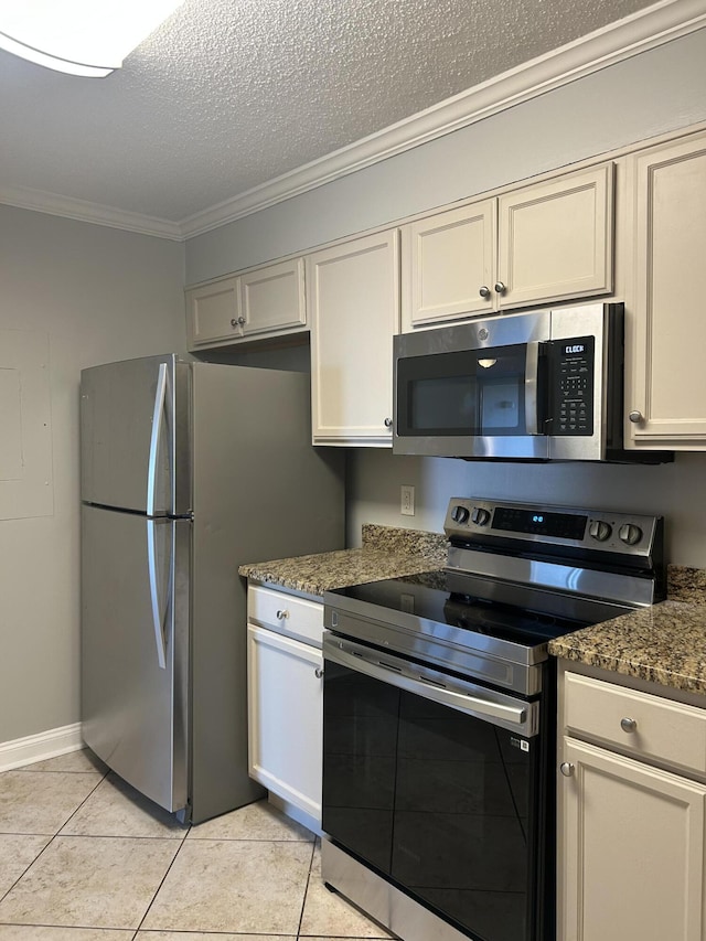 kitchen with light tile patterned flooring, dark stone countertops, ornamental molding, and appliances with stainless steel finishes