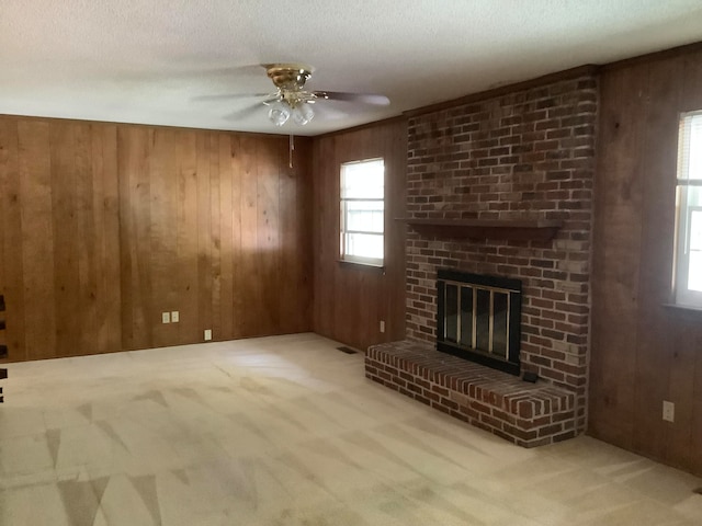 unfurnished living room with a fireplace, light colored carpet, wooden walls, and ceiling fan