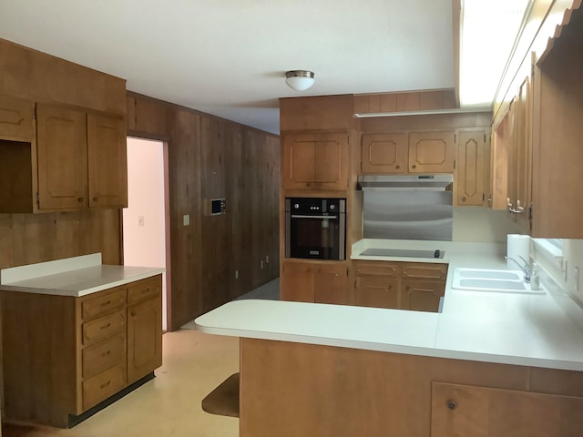 kitchen with kitchen peninsula, black appliances, sink, and wooden walls