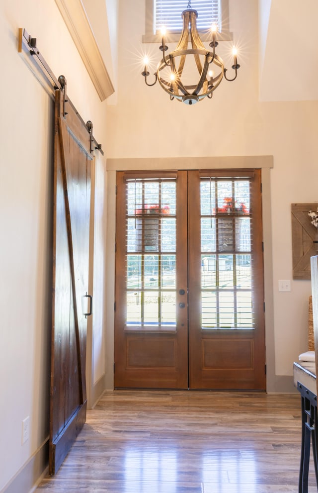 doorway to outside with french doors, light hardwood / wood-style flooring, a notable chandelier, and a barn door