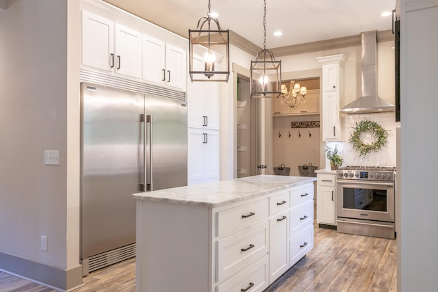 kitchen with wall chimney range hood, hanging light fixtures, a center island, premium appliances, and white cabinetry