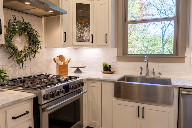 kitchen featuring range hood, light stone countertops, appliances with stainless steel finishes, and decorative backsplash