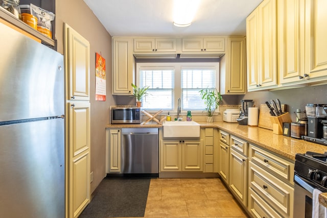 kitchen featuring stainless steel appliances, light tile patterned floors, sink, and light stone counters