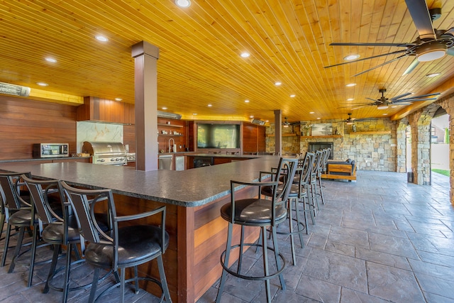 kitchen featuring wood ceiling, ornate columns, a breakfast bar area, kitchen peninsula, and ceiling fan