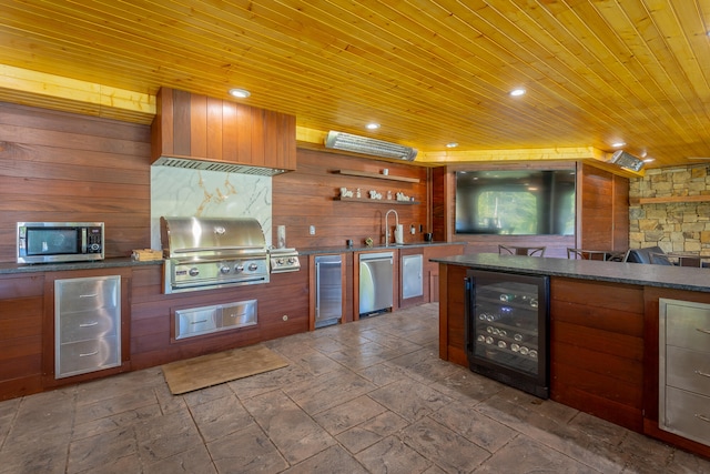 kitchen featuring sink, wood ceiling, stainless steel appliances, wooden walls, and beverage cooler