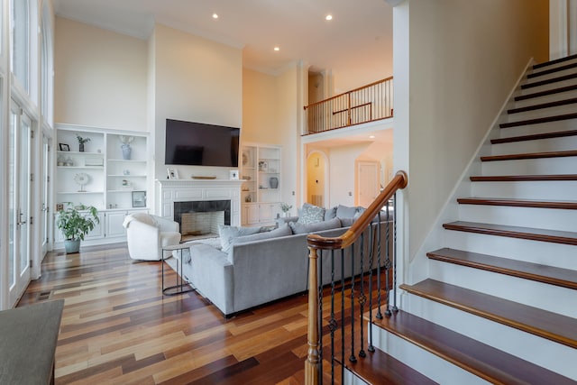 living room featuring hardwood / wood-style flooring, ornamental molding, a high ceiling, and built in features