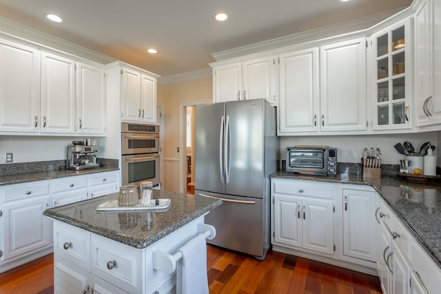 kitchen featuring white cabinets, appliances with stainless steel finishes, dark stone counters, ornamental molding, and dark wood-type flooring