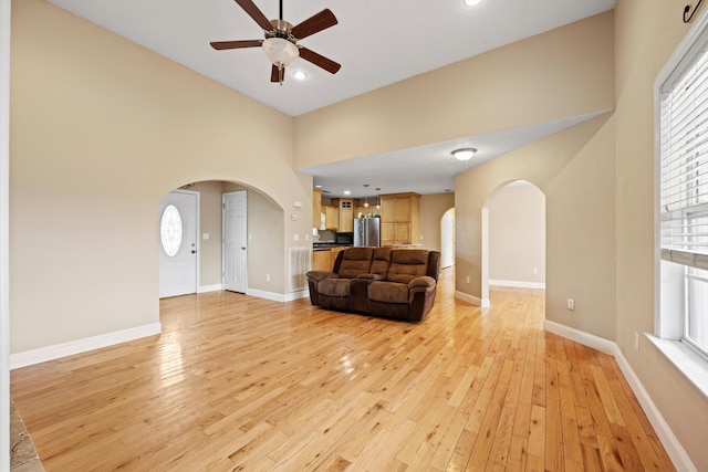 living room with a high ceiling, ceiling fan, and light hardwood / wood-style floors