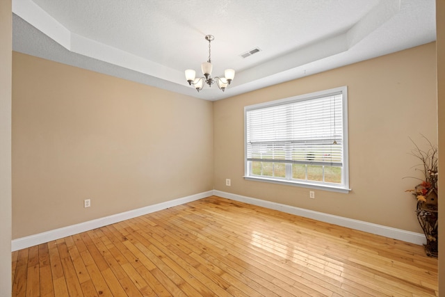 unfurnished room with a textured ceiling, a notable chandelier, light hardwood / wood-style floors, and a raised ceiling