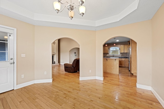 interior space featuring light wood-type flooring, sink, a raised ceiling, and an inviting chandelier