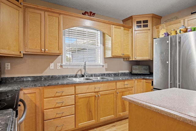 kitchen with appliances with stainless steel finishes, a textured ceiling, light brown cabinets, sink, and light hardwood / wood-style flooring