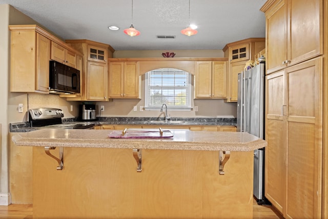 kitchen featuring sink, a breakfast bar, appliances with stainless steel finishes, light hardwood / wood-style flooring, and pendant lighting