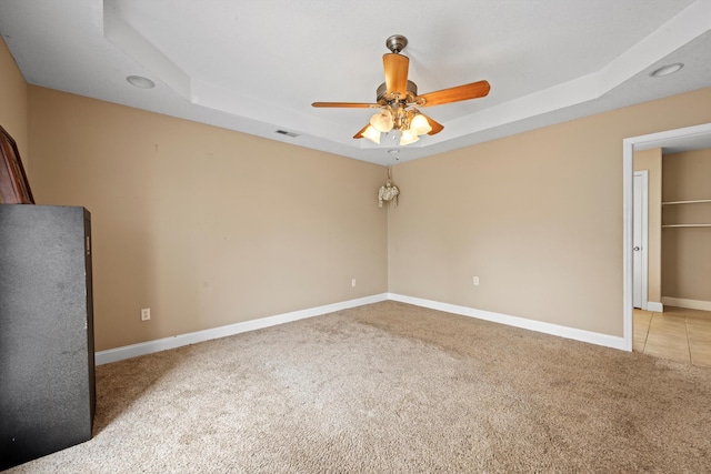 unfurnished bedroom with a walk in closet, a tray ceiling, light colored carpet, and ceiling fan