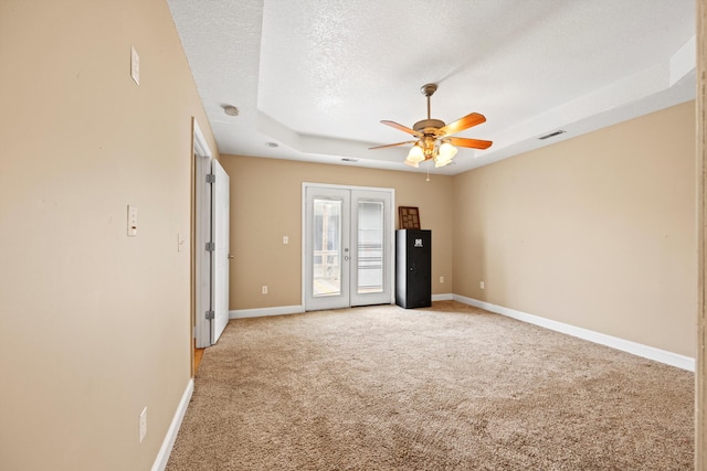 carpeted empty room featuring ceiling fan, a textured ceiling, french doors, and a tray ceiling