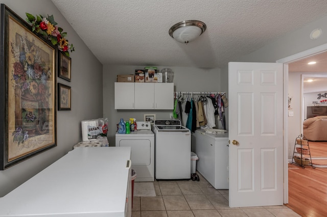 clothes washing area featuring washer and dryer, light tile patterned flooring, a textured ceiling, and cabinets