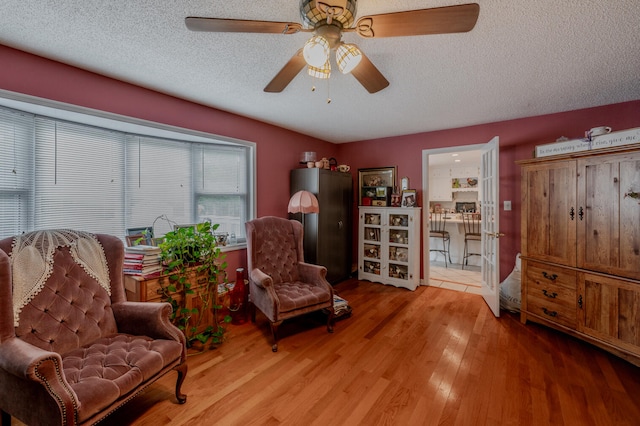 living area featuring ceiling fan, a textured ceiling, and light hardwood / wood-style flooring