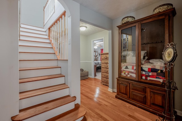 stairway featuring a textured ceiling, wood-type flooring, and ceiling fan