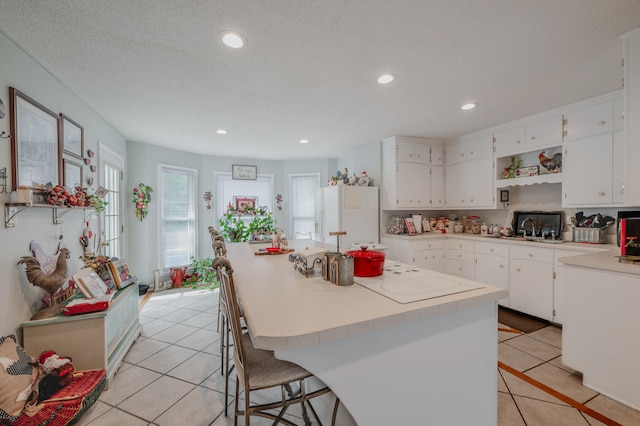 kitchen with white fridge with ice dispenser, a kitchen island, a textured ceiling, white cabinetry, and light tile patterned floors