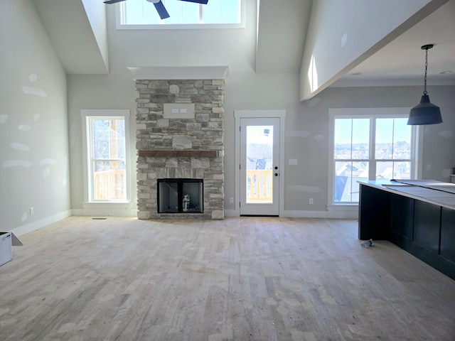 unfurnished living room with a stone fireplace, light hardwood / wood-style flooring, ceiling fan, and a high ceiling