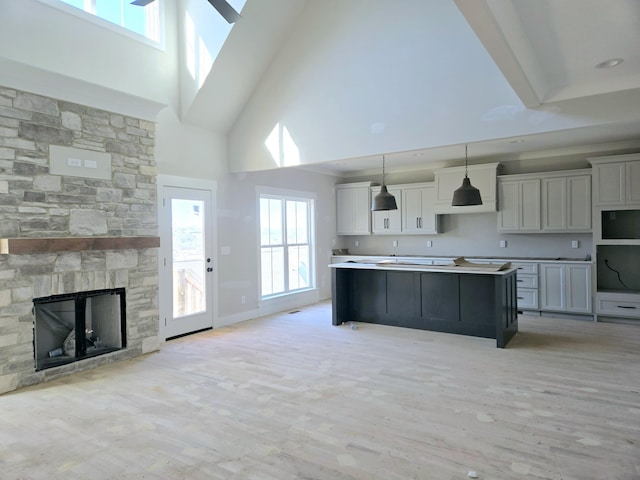 kitchen featuring gray cabinets, a center island, a fireplace, decorative light fixtures, and light wood-type flooring