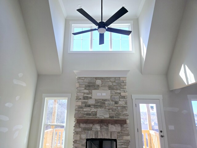 unfurnished living room featuring a high ceiling, crown molding, a stone fireplace, and ceiling fan