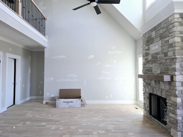 unfurnished living room with a fireplace, light hardwood / wood-style flooring, ceiling fan, and a high ceiling