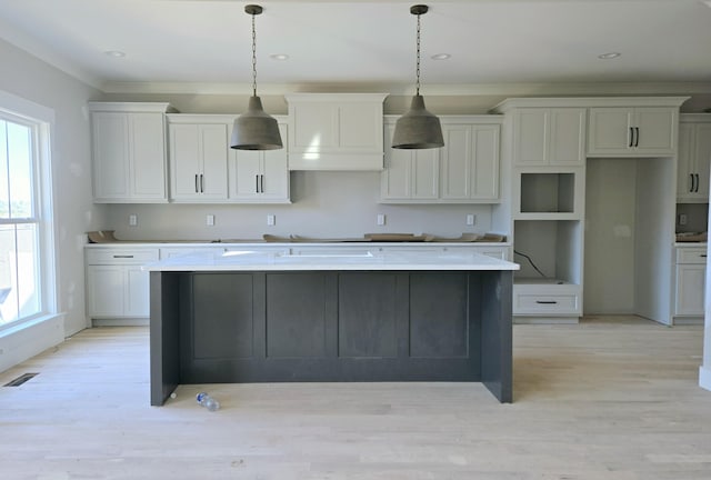 kitchen with light wood-type flooring, a kitchen island with sink, hanging light fixtures, and white cabinets